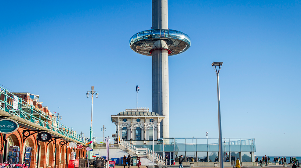 Brighton i360 tower with the glass pod and colorful shops nearby in a sunny day.